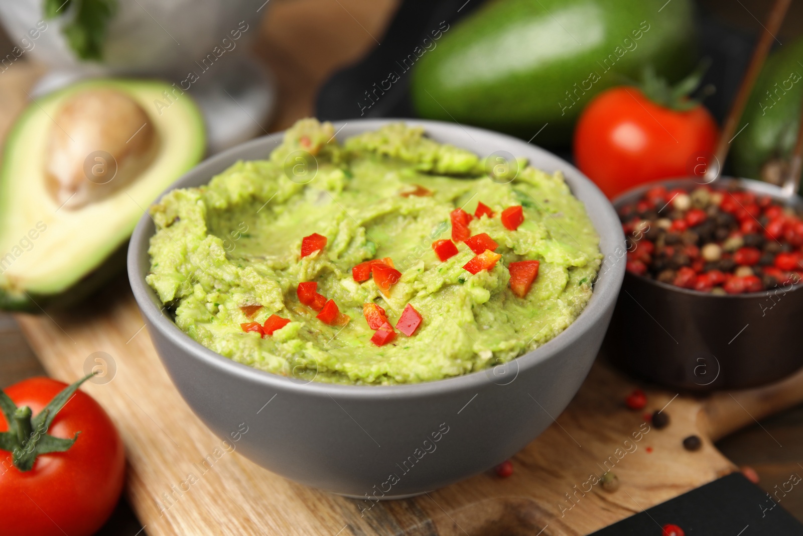 Photo of Bowl of delicious guacamole and ingredients on wooden board, closeup