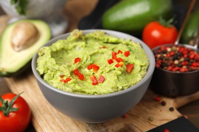 Photo of Bowl of delicious guacamole and ingredients on wooden board, closeup