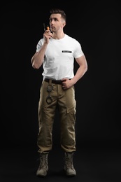 Male security guard using portable radio transmitter on dark background