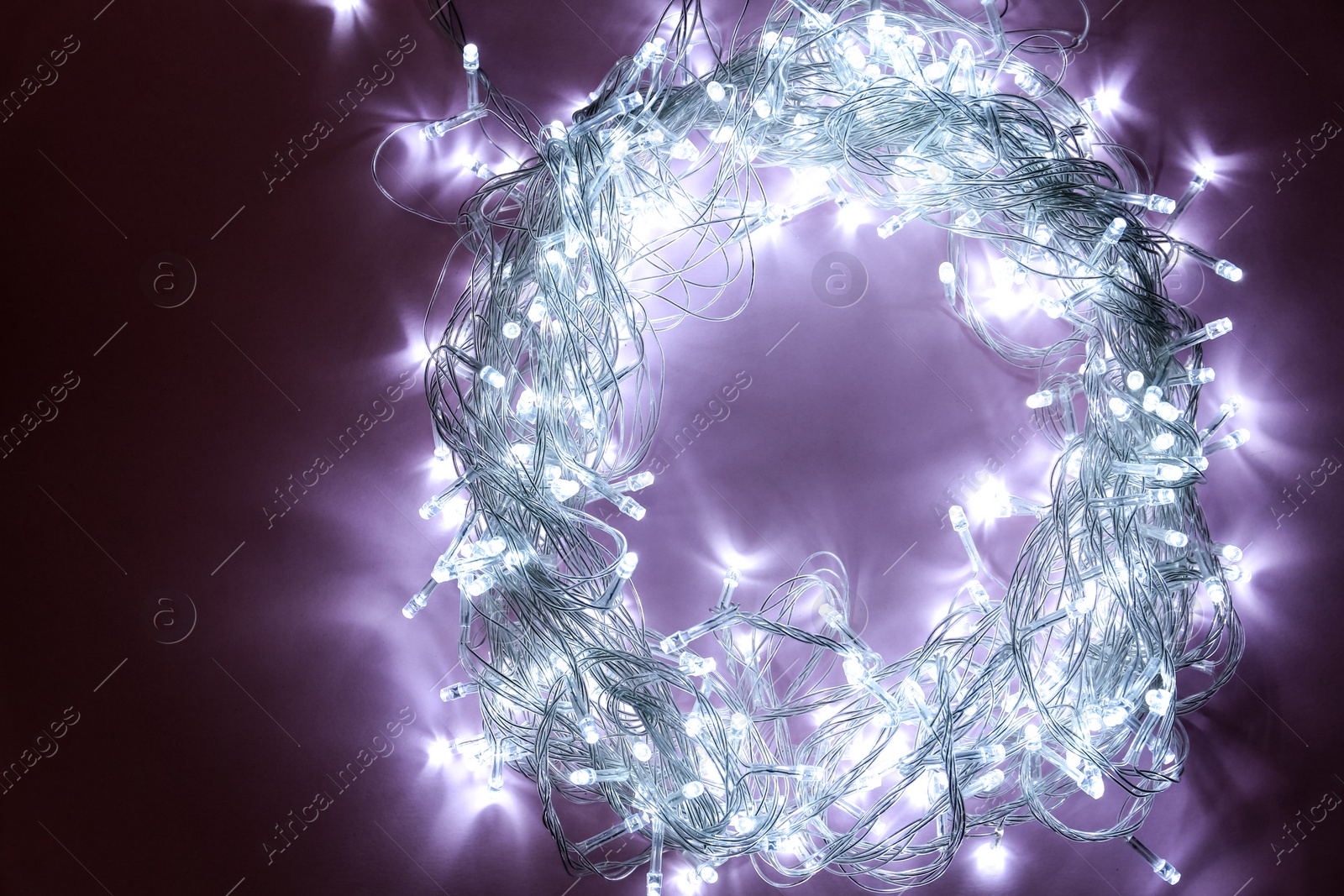 Photo of Glowing Christmas lights on violet background, top view