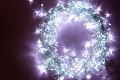 Photo of Glowing Christmas lights on violet background, top view