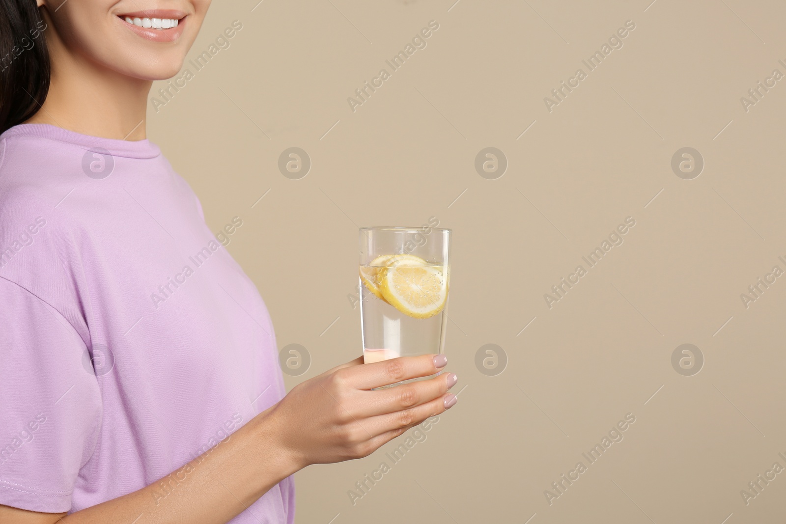 Photo of Woman with tasty lemon water on beige background, closeup. Space for text