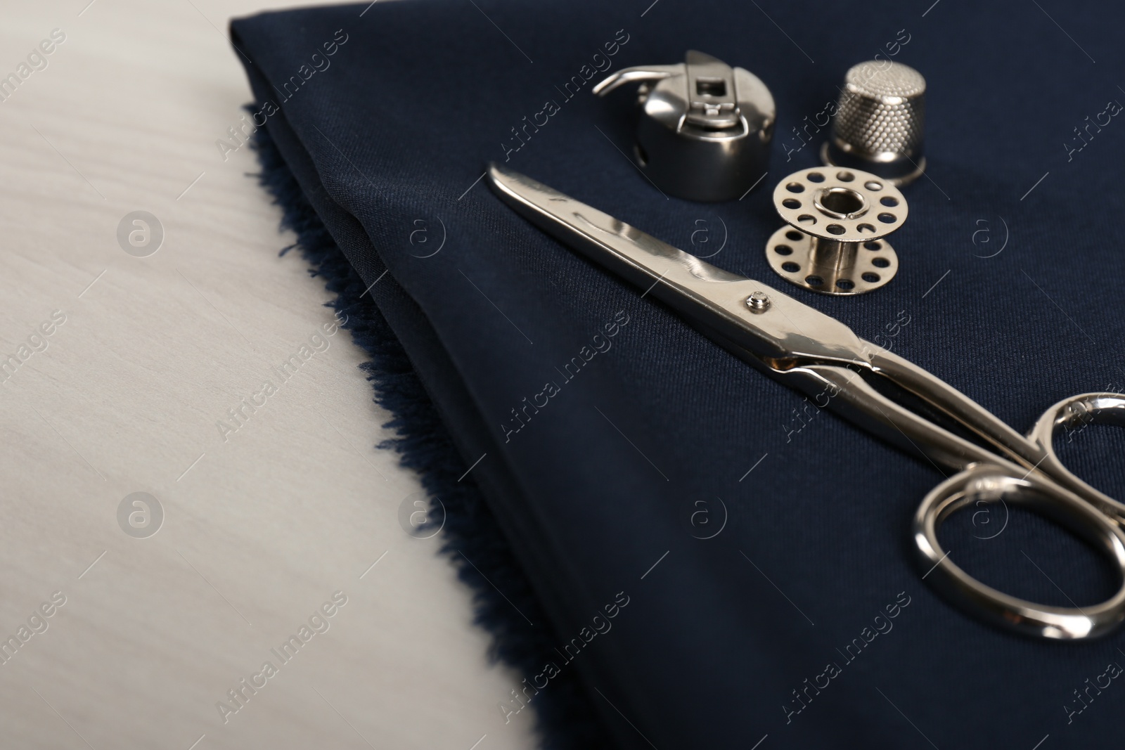 Photo of Different sewing items and fabric on light beige wooden table, closeup