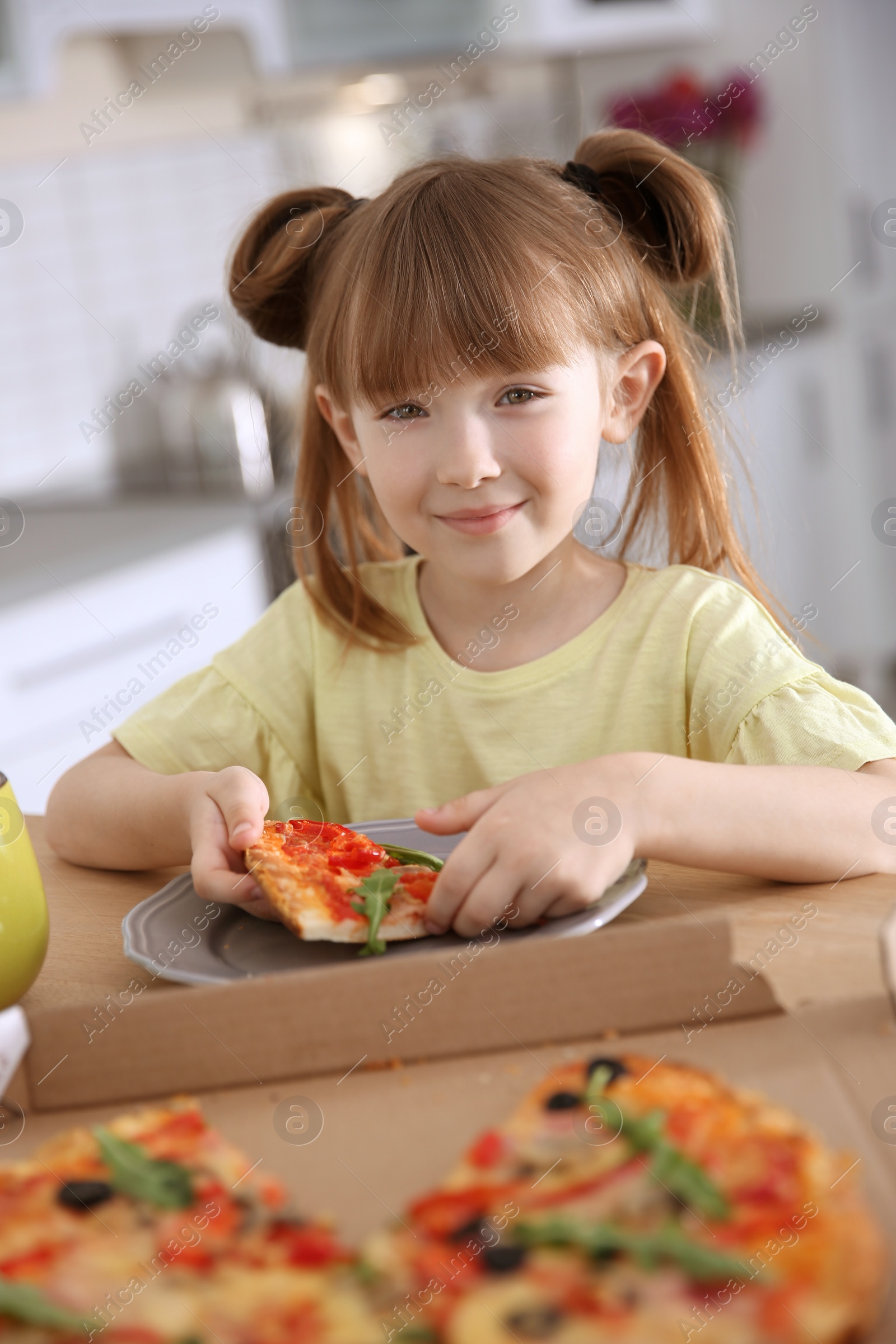 Photo of Cute little girl eating tasty pizza at home