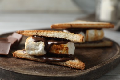 Photo of Delicious marshmallow sandwiches with chocolate on wooden tray, closeup
