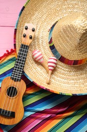 Photo of Mexican sombrero hat, guitar, maracas and colorful poncho on pink background, flat lay