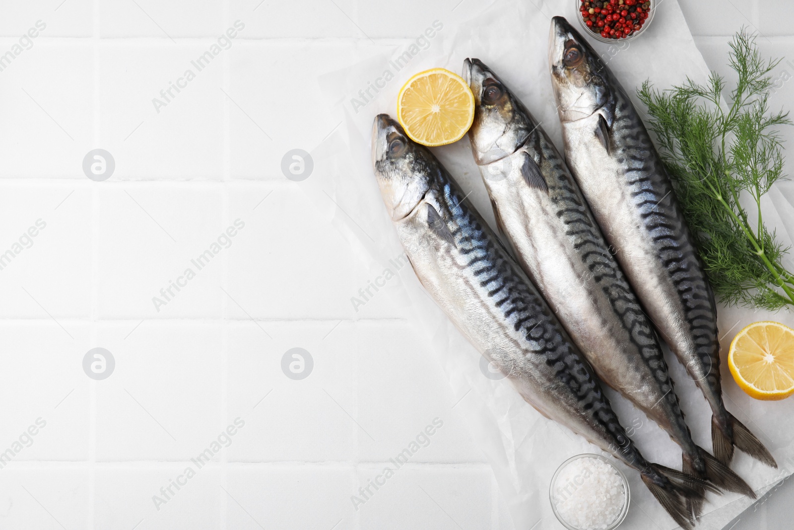 Photo of Tasty salted mackerels, spices and cut lemons on white tiled table, flat lay. Space for text