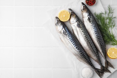 Photo of Tasty salted mackerels, spices and cut lemons on white tiled table, flat lay. Space for text