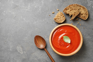 Bowl of fresh homemade tomato soup and bread on grey background, top view. Space for text