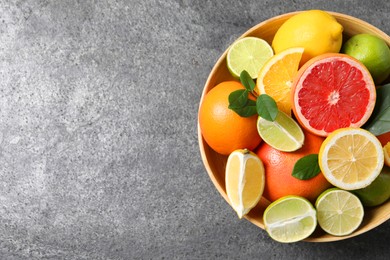 Photo of Different fresh citrus fruits and leaves in bowl on grey textured table, top view. Space for text