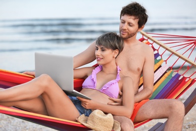 Photo of Young couple resting with laptop in hammock on beach