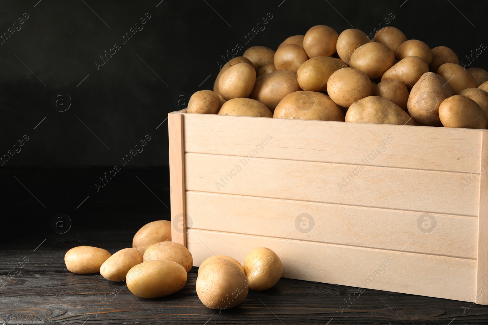 Photo of Raw fresh organic potatoes on wooden table against dark background