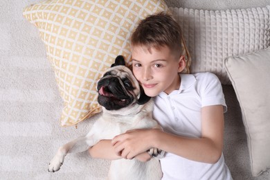 Boy with his cute pug lying on floor at home, top view