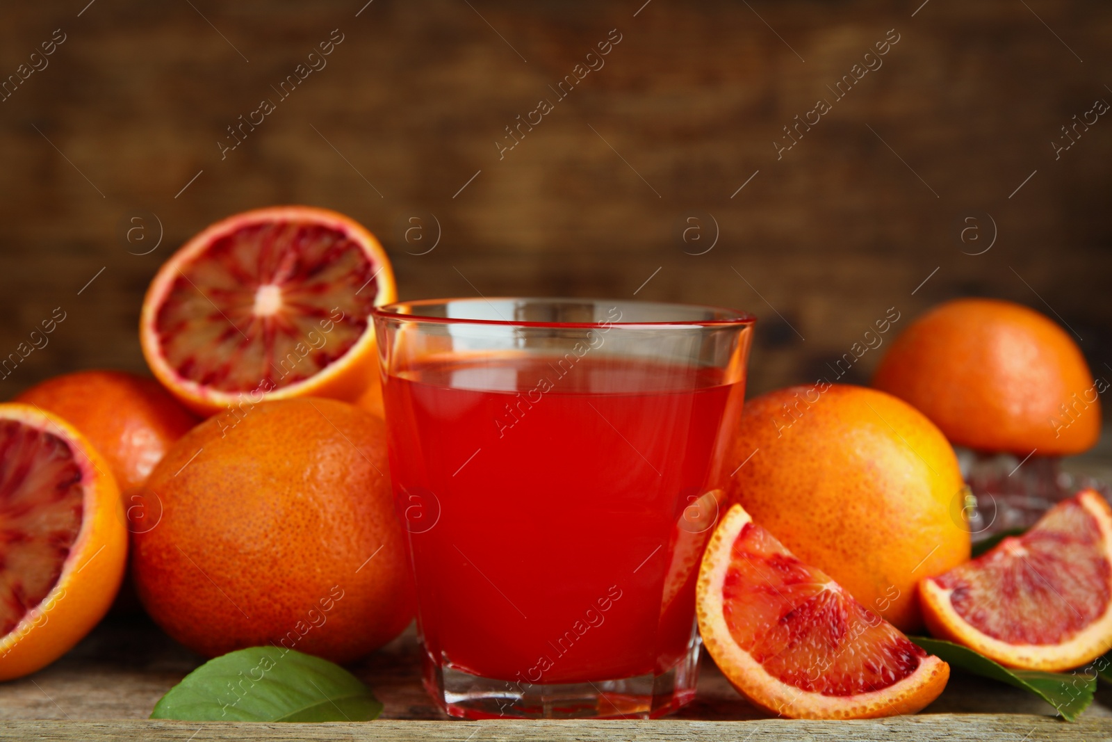 Photo of Tasty sicilian orange juice in glass and fruits on wooden table