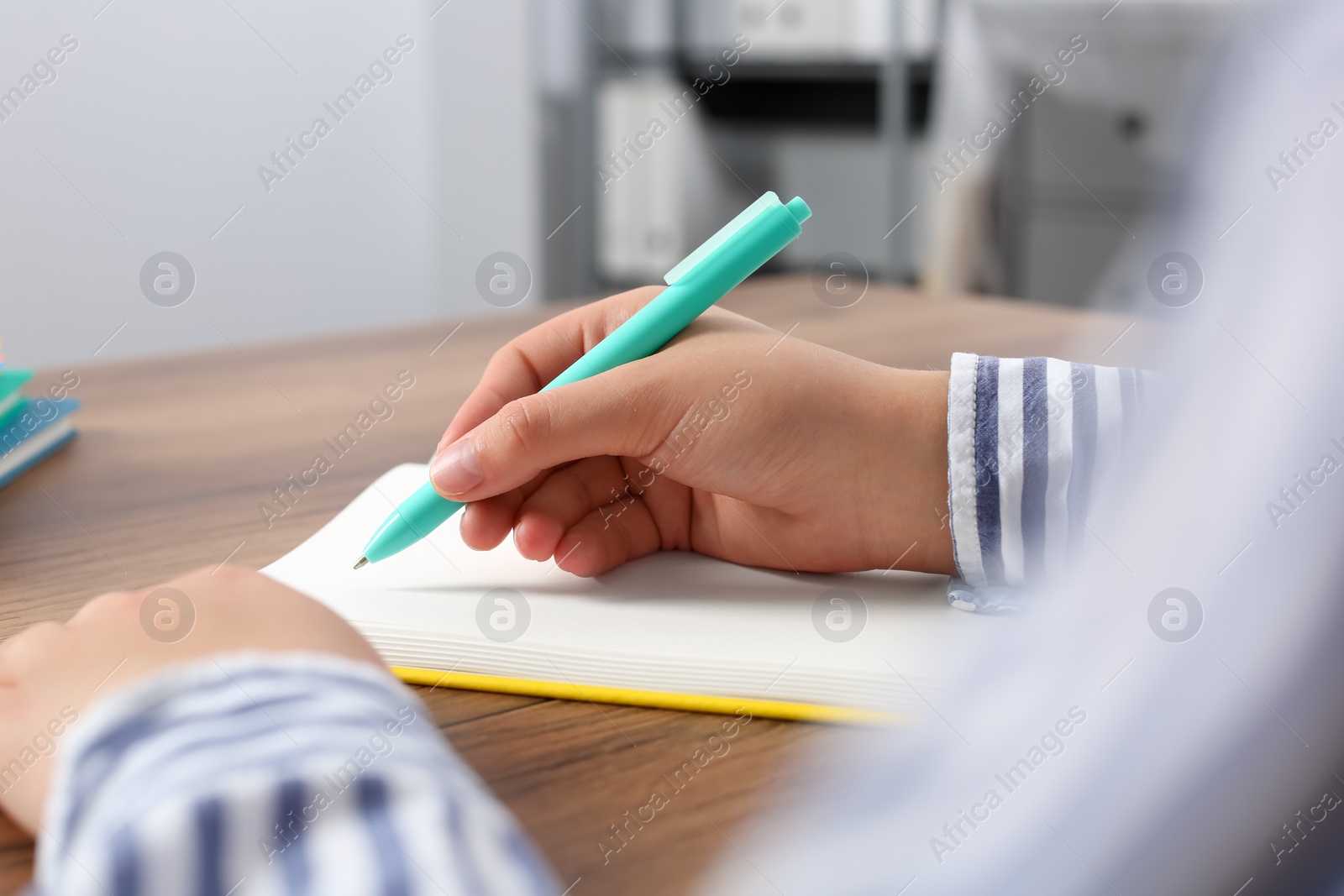 Photo of Woman writing in notebook at wooden table indoors, closeup