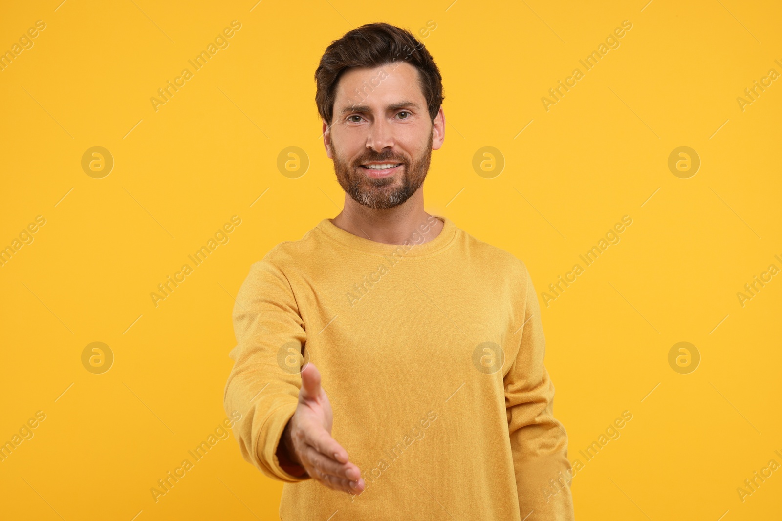 Photo of Happy man welcoming and offering handshake on orange background