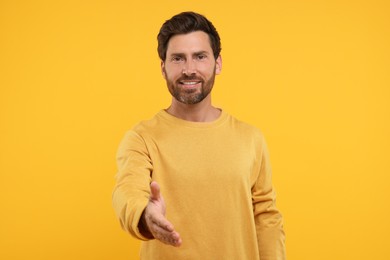 Photo of Happy man welcoming and offering handshake on orange background