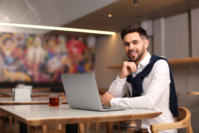 Photo of Young male business owner working with laptop in his cafe