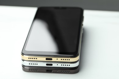 Stack of modern smartphones on white table, closeup