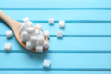 Photo of Spoon with refined sugar cubes on color wooden background