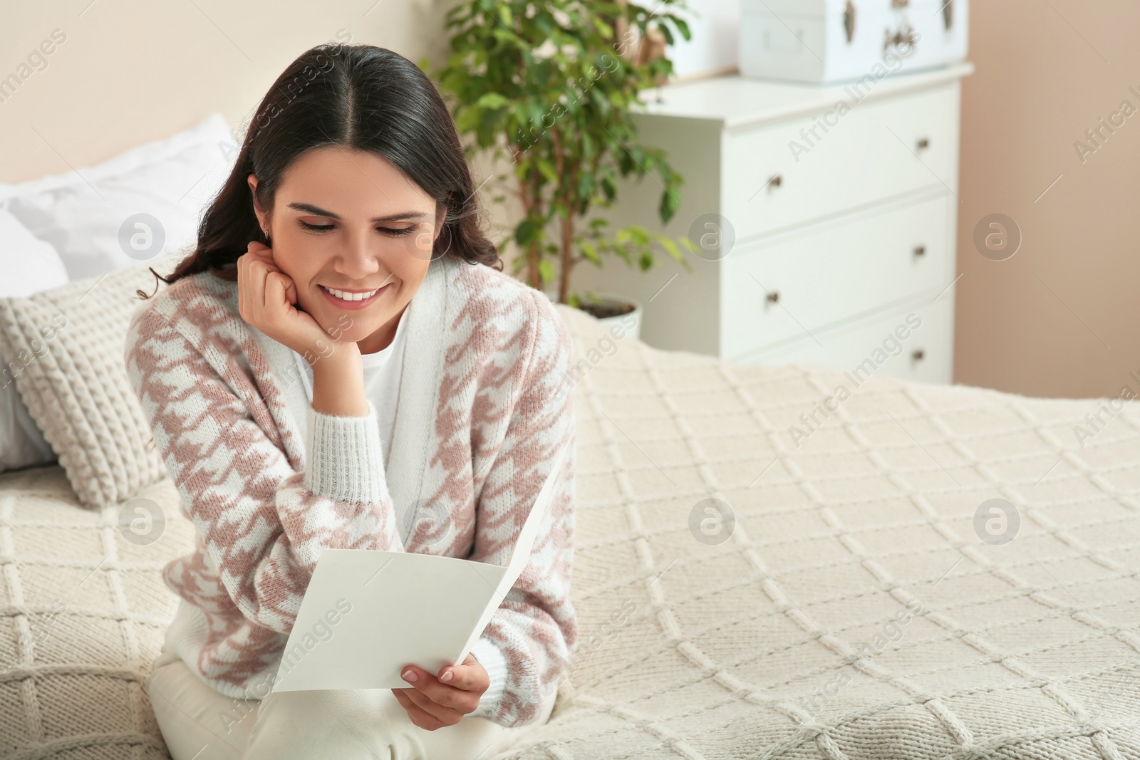 Photo of Young woman with greeting card on bed in room, space for text