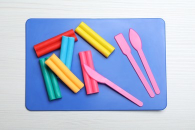 Photo of Many different colorful plasticine pieces with tools on white wooden table, top view