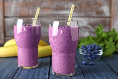 Glasses of delicious blueberry smoothie on blue wooden table