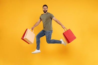 Photo of Happy man with many paper shopping bags jumping on orange background