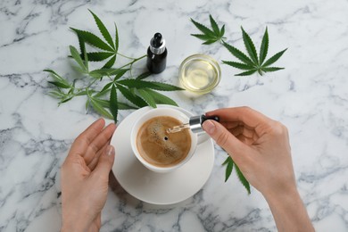 Photo of Top view of woman dripping THC tincture or CBD oil into coffee at white marble table, closeup