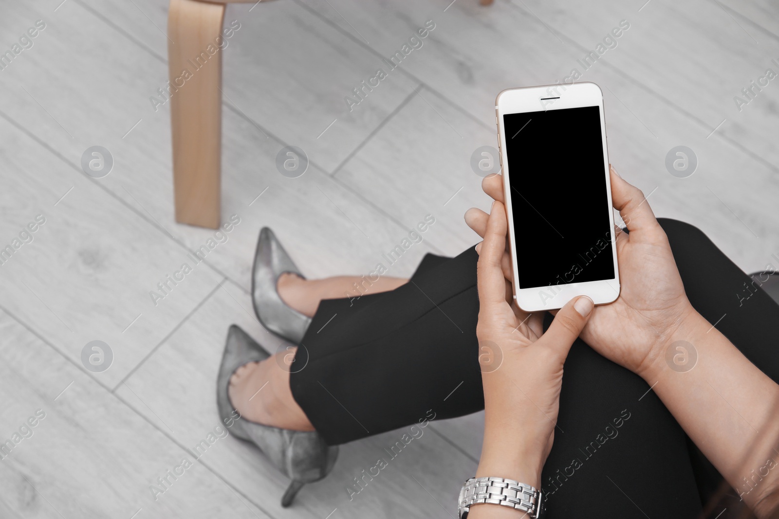 Photo of Young woman holding mobile phone with blank screen in hands indoors