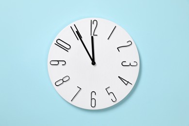 Stylish analog clock hanging on light blue wall. New Year countdown