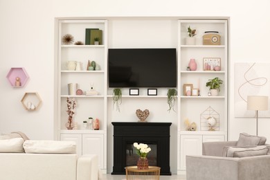 Photo of Stylish room interior with beautiful fireplace, TV set, sofa, armchairs and shelves with decor