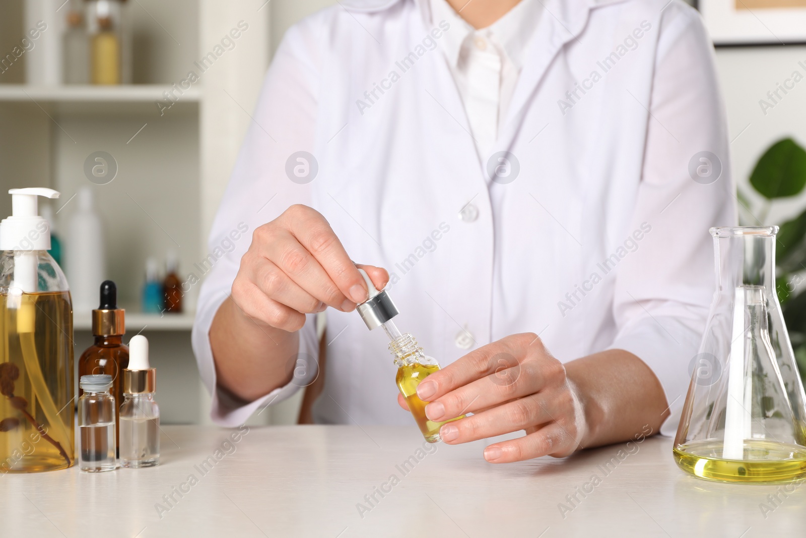 Photo of Dermatologist developing cosmetic oil at white table indoors, closeup