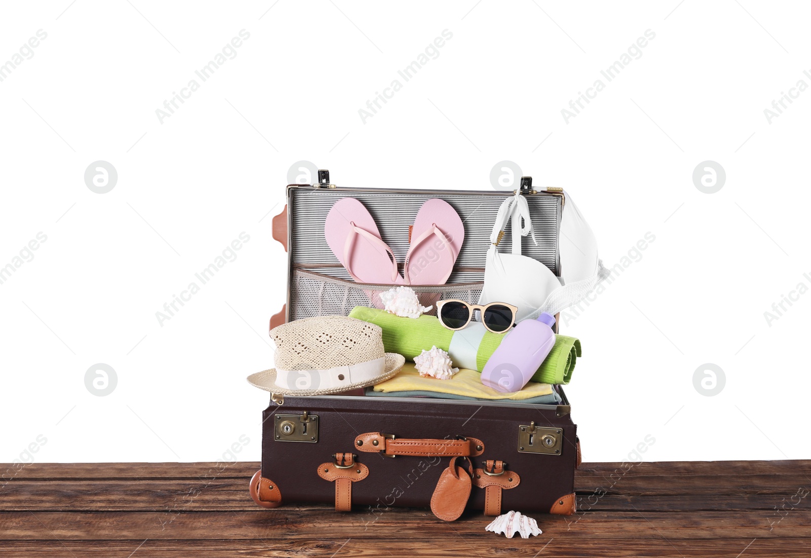 Photo of Open vintage suitcase with different beach objects packed for summer vacation on wooden table against white background