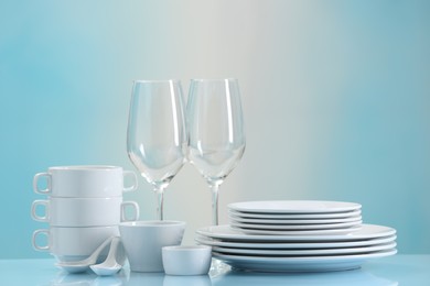 Set of many clean dishware and glasses on light blue table