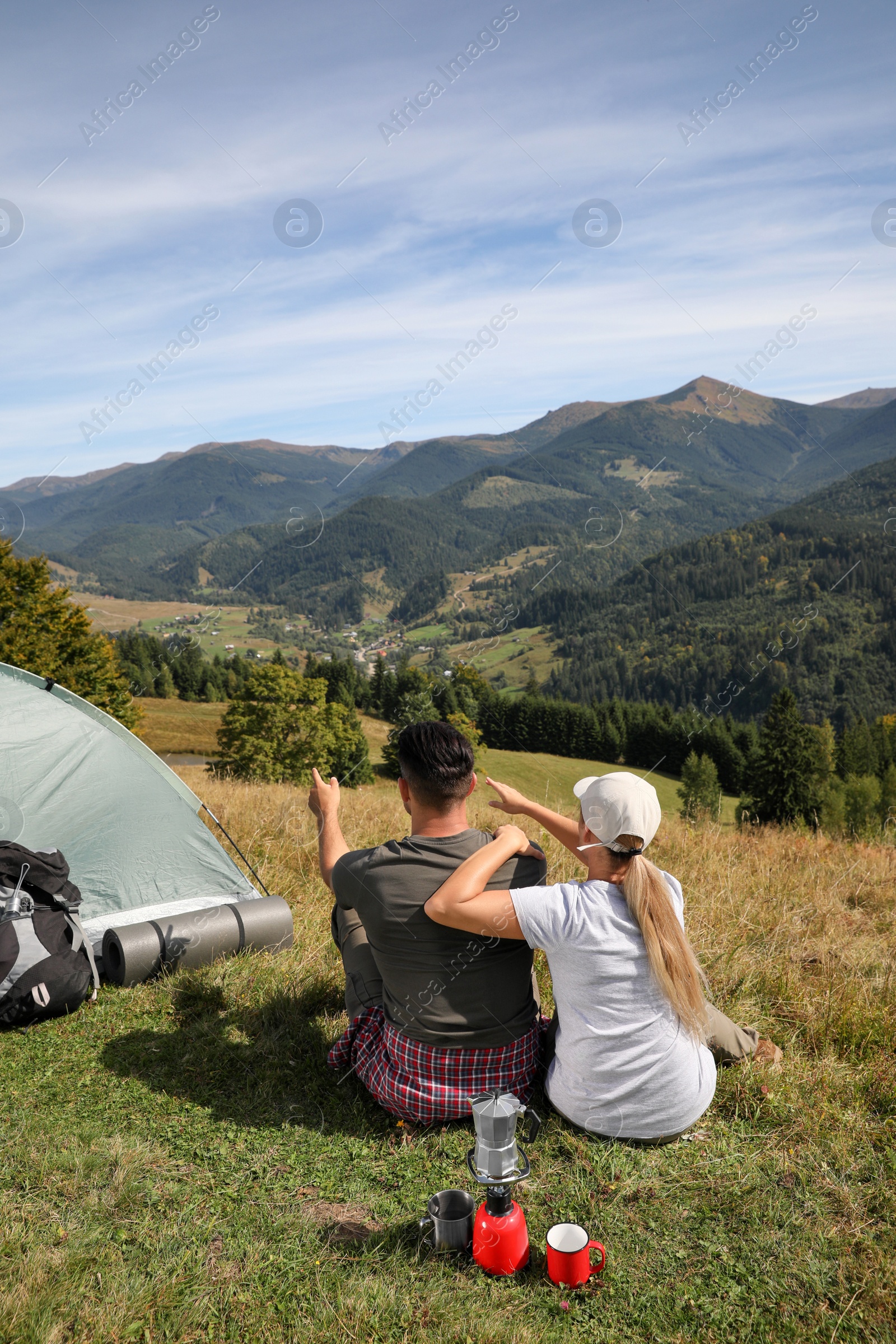 Photo of Couple enjoying mountain landscape near camping tent, back view