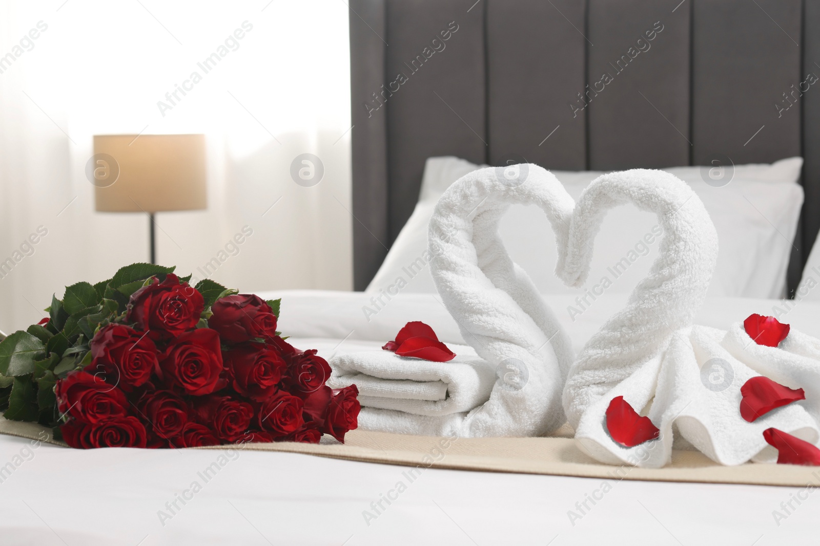 Photo of Honeymoon. Swans made of towels and beautiful red roses on bed in room