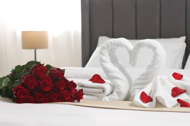 Honeymoon. Swans made of towels and beautiful red roses on bed in room