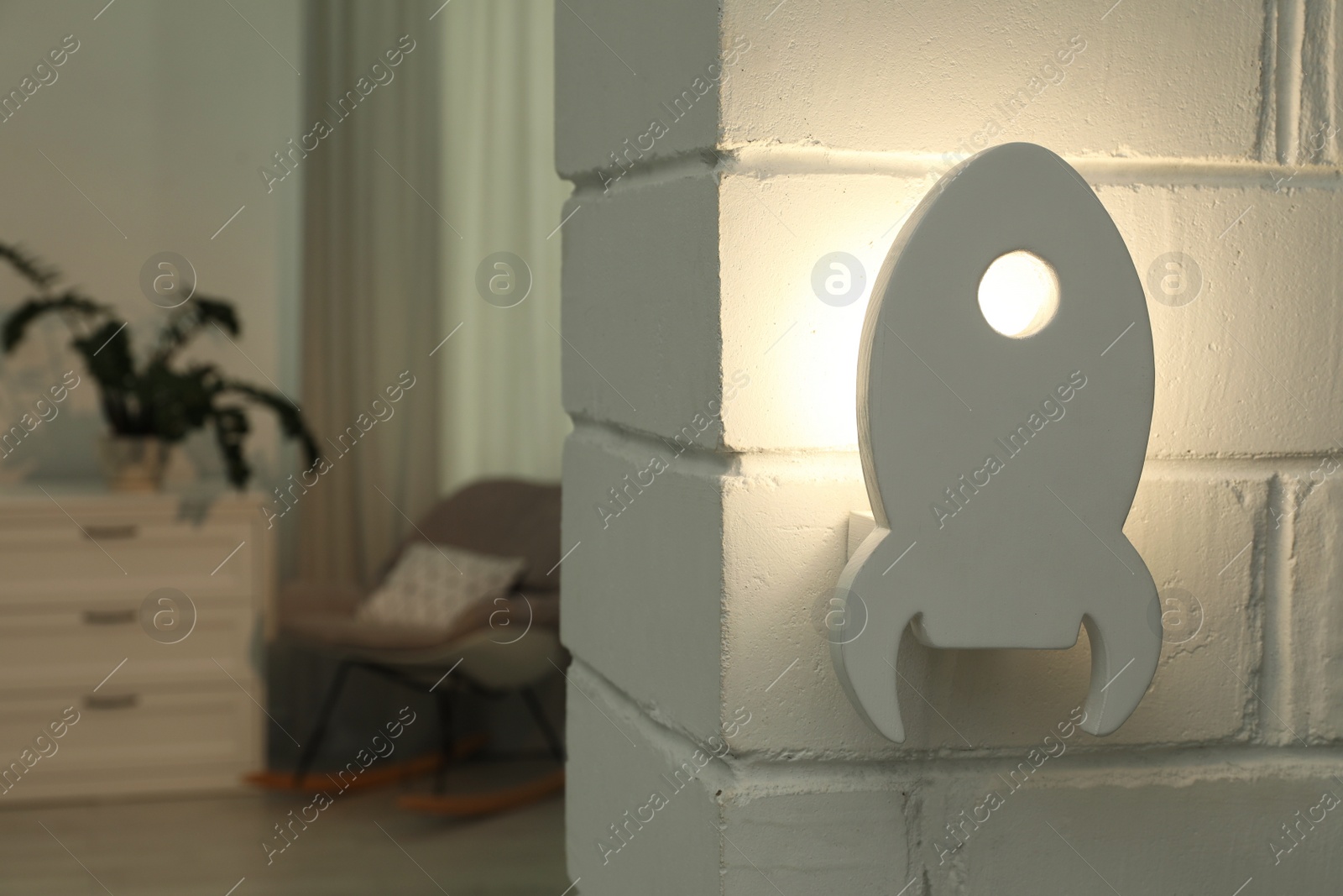 Photo of Rocket shaped night lamp on white brick wall in child's room