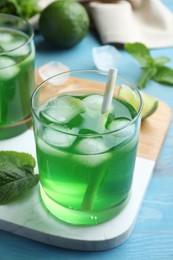 Delicious mint liqueur with green leaves and ice cubes on turquoise wooden table, closeup