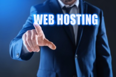 Image of Businessman pointing at phrase WEB HOSTING on virtual screen against dark background, focus on hand