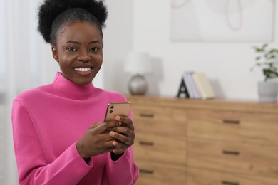 Photo of Happy young woman using smartphone at home. Space for text