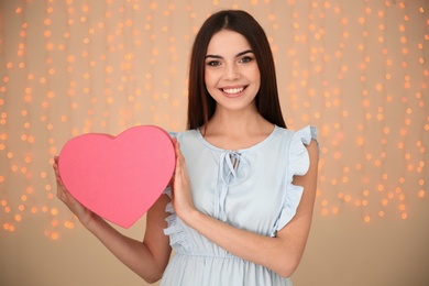 Portrait of beautiful smiling girl with heart shaped gift box on blurred background. International Women's Day