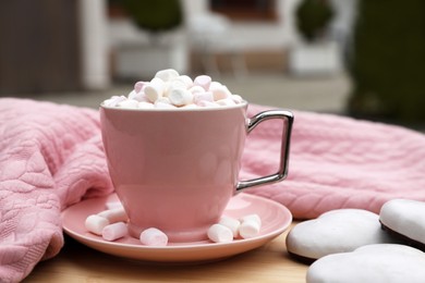 Photo of Cup of tasty cocoa with marshmallows, pink sweater and cookies on wooden table outdoors