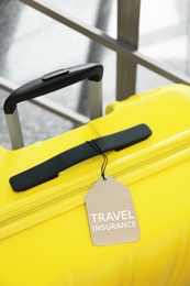 Photo of Yellow suitcase with TRAVEL INSURANCE label at stairs indoors, closeup