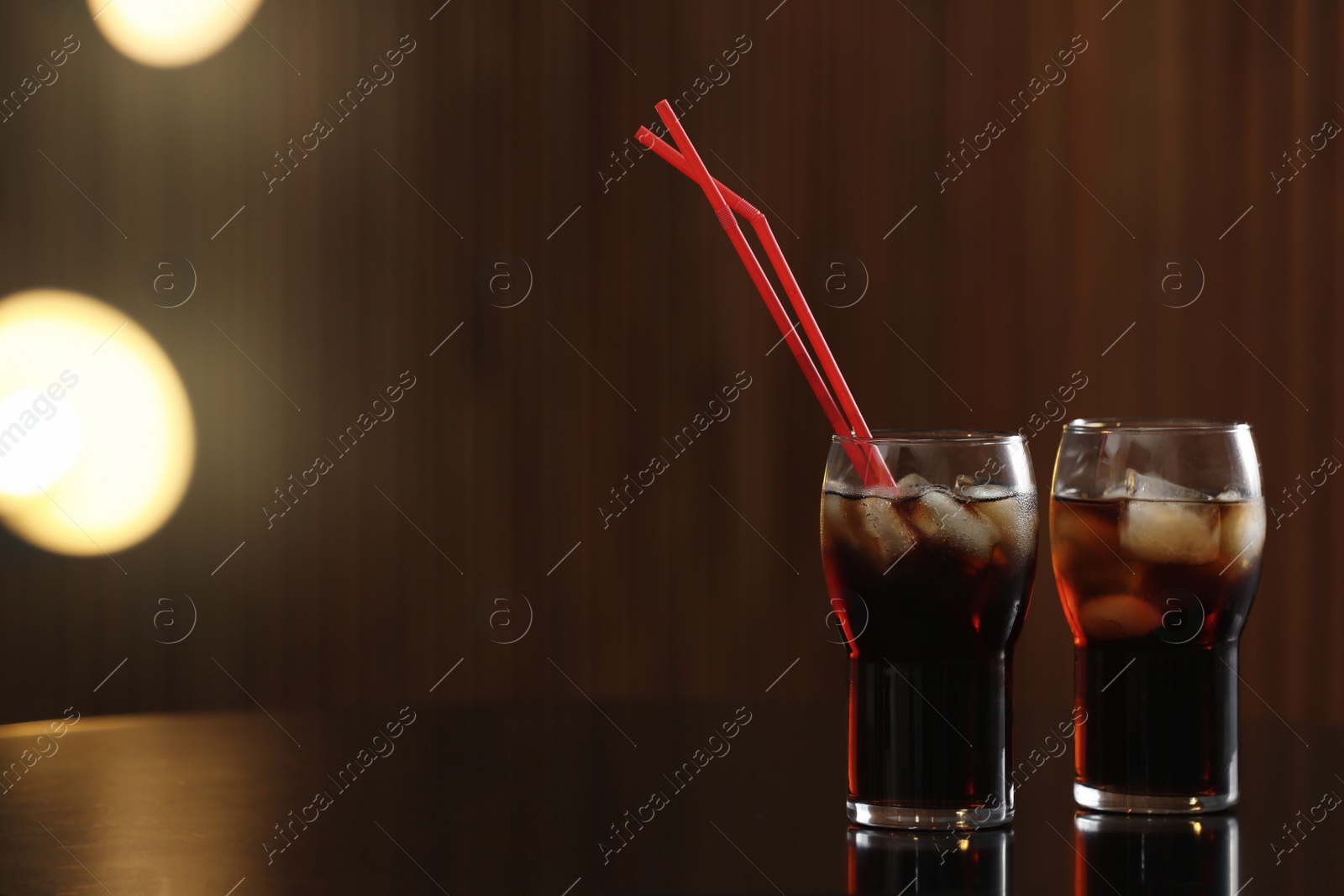 Photo of Glasses of cola with ice on table against blurred background. Space for text