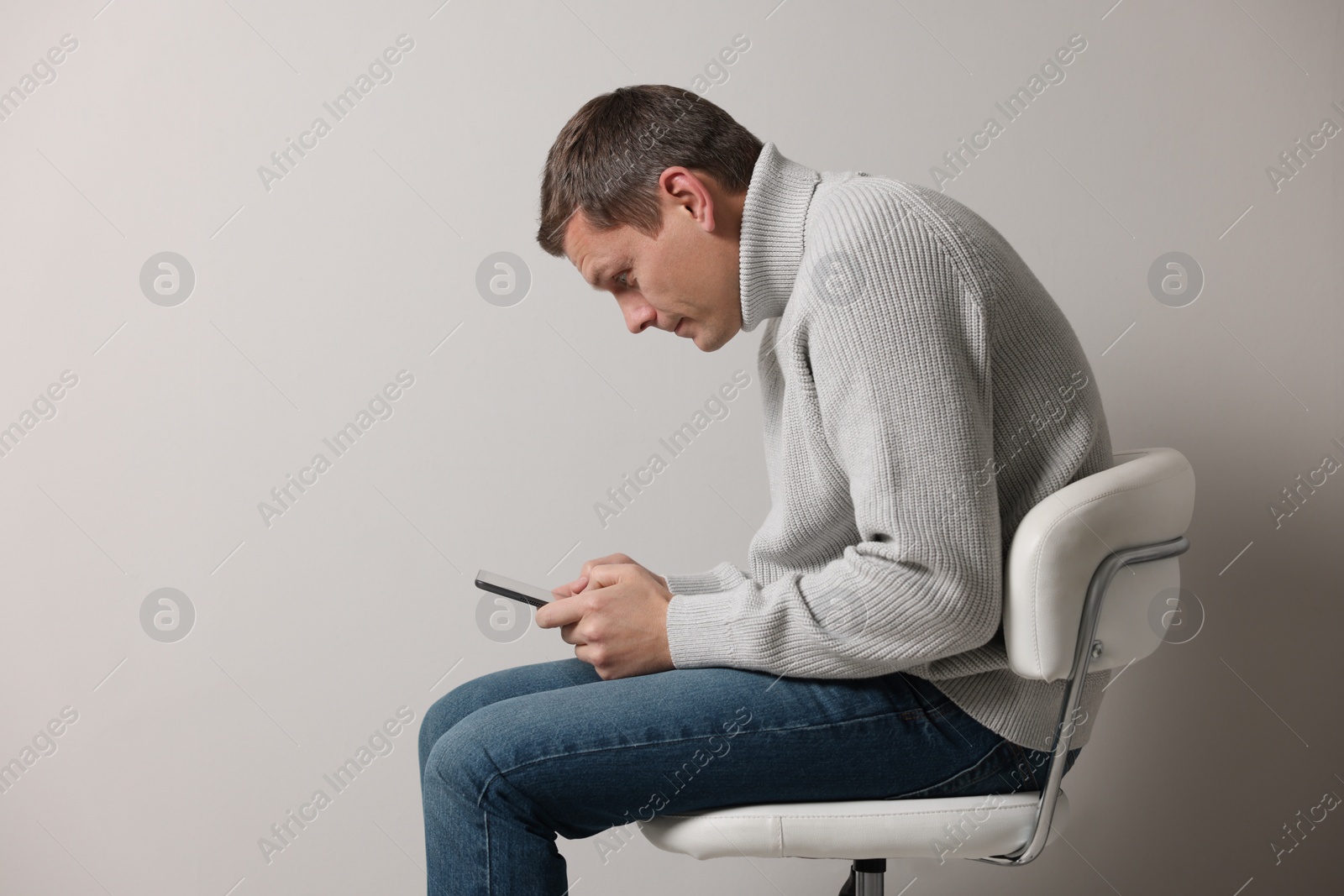 Photo of Man with bad posture using tablet while sitting on chair against grey background. Space for text