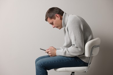 Man with bad posture using tablet while sitting on chair against grey background. Space for text