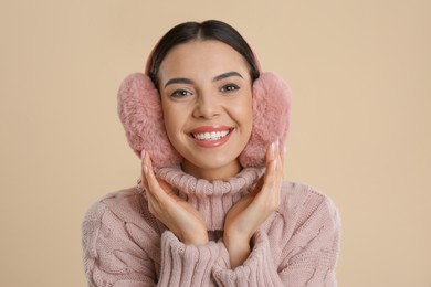 Photo of Beautiful young woman wearing earmuffs on beige background