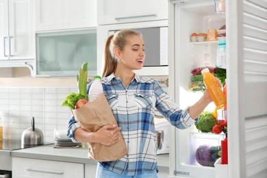 Photo of Woman putting products into refrigerator in kitchen